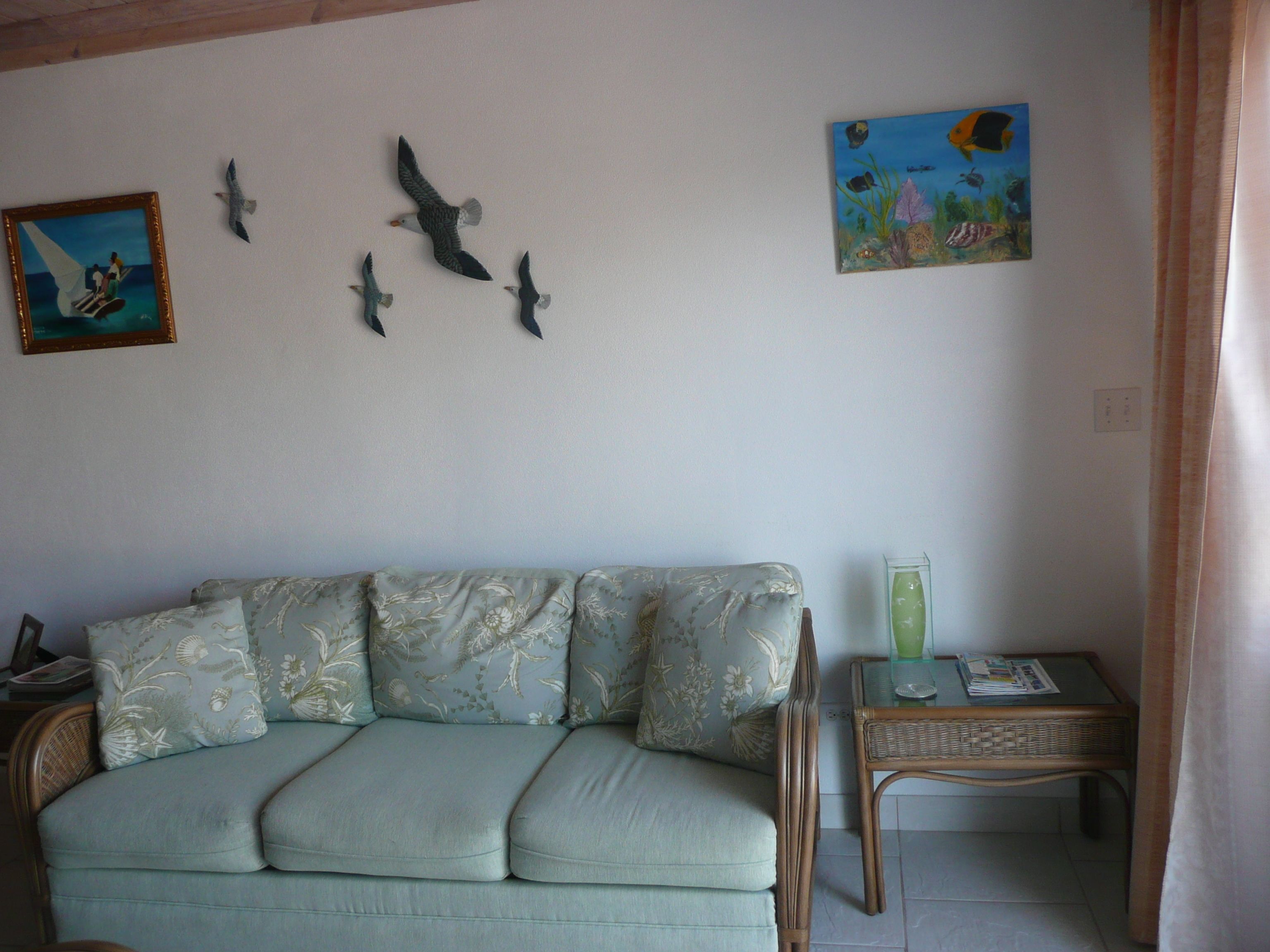 Un salón con sofá, una mesita y adornos en la pared, incluyendo un cuadro y esculturas de pájaros.