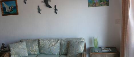 Un salón con sofá, una mesita y adornos en la pared, incluyendo un cuadro y esculturas de pájaros.