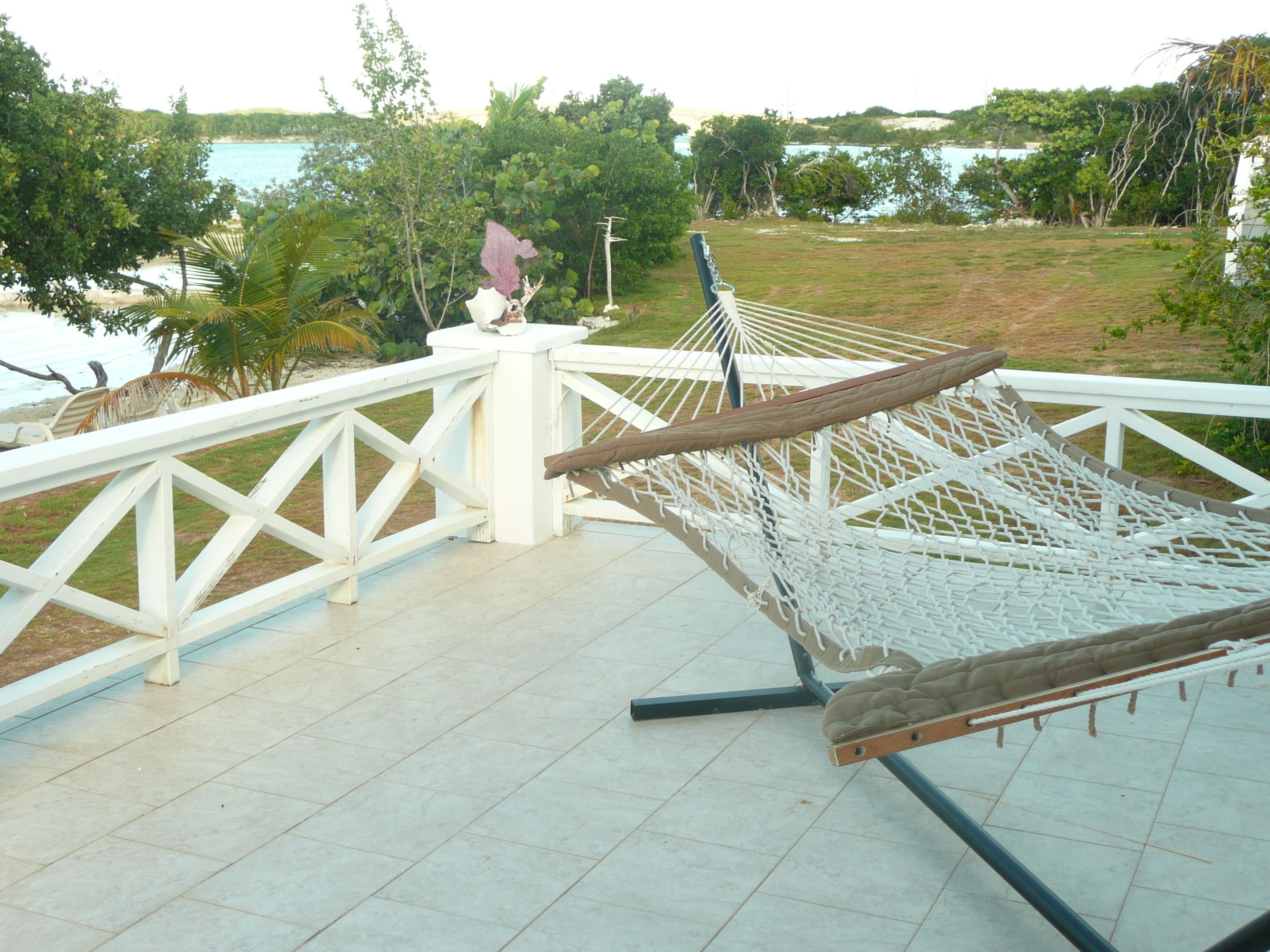 A hammock on a white metal deck with a view of a beach and ocean.