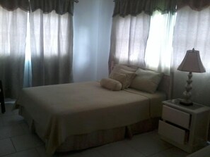 A bedroom with a bed, curtains, a nightstand, and a lamp.