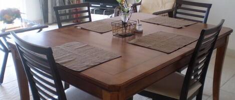 Een eethoek met een houten tafel, vier stoelen en een televisie op de achtergrond.