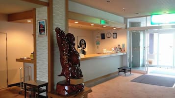A reception area with a wooden sculpture, a reception desk, a bench, and a door leading outside.