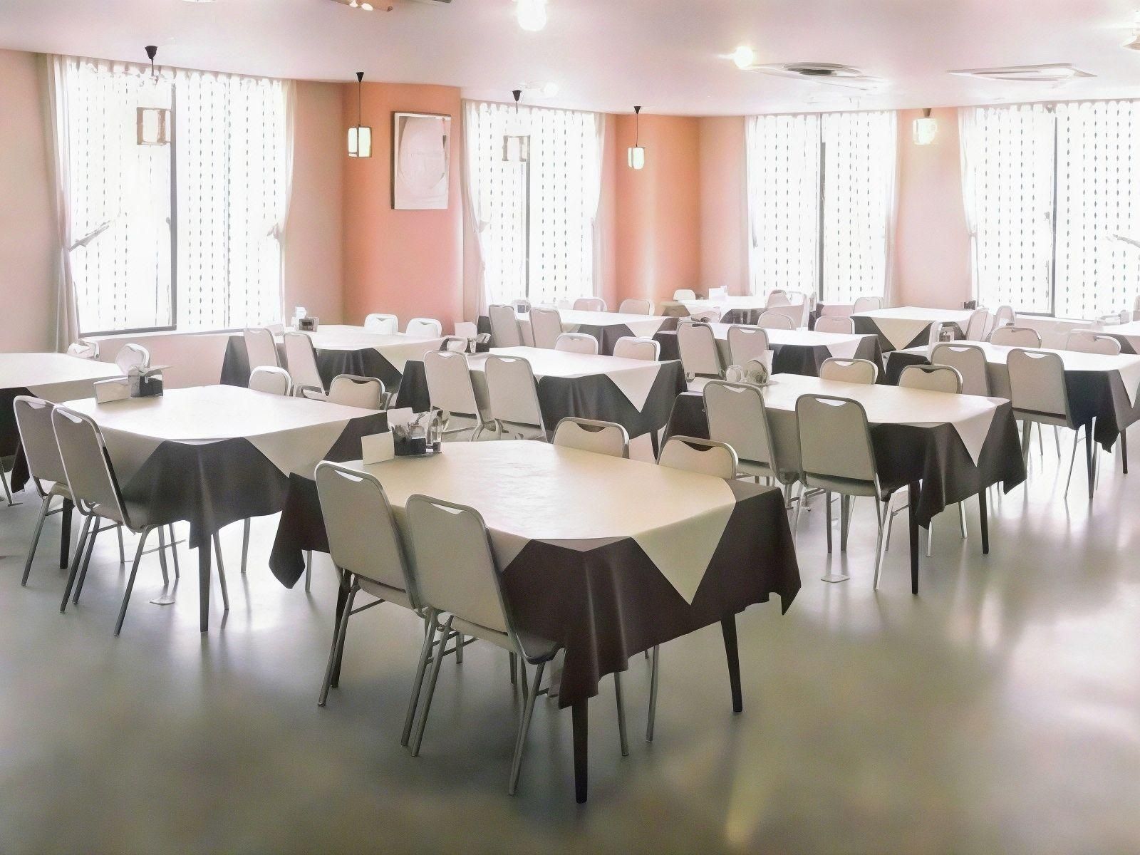 A conference room with multiple tables and chairs, large windows with blinds, and ceiling lights.