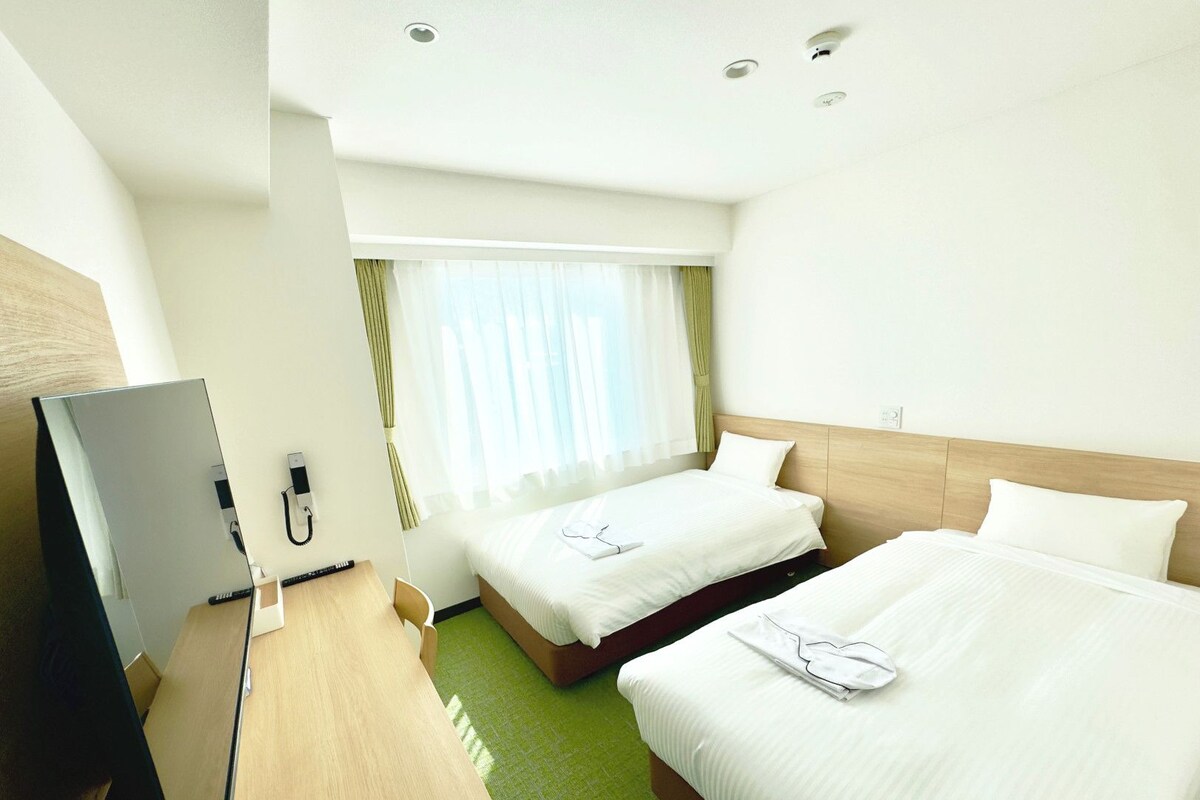Une chambre d’hôtel avec deux lits, un bureau et une télévision.