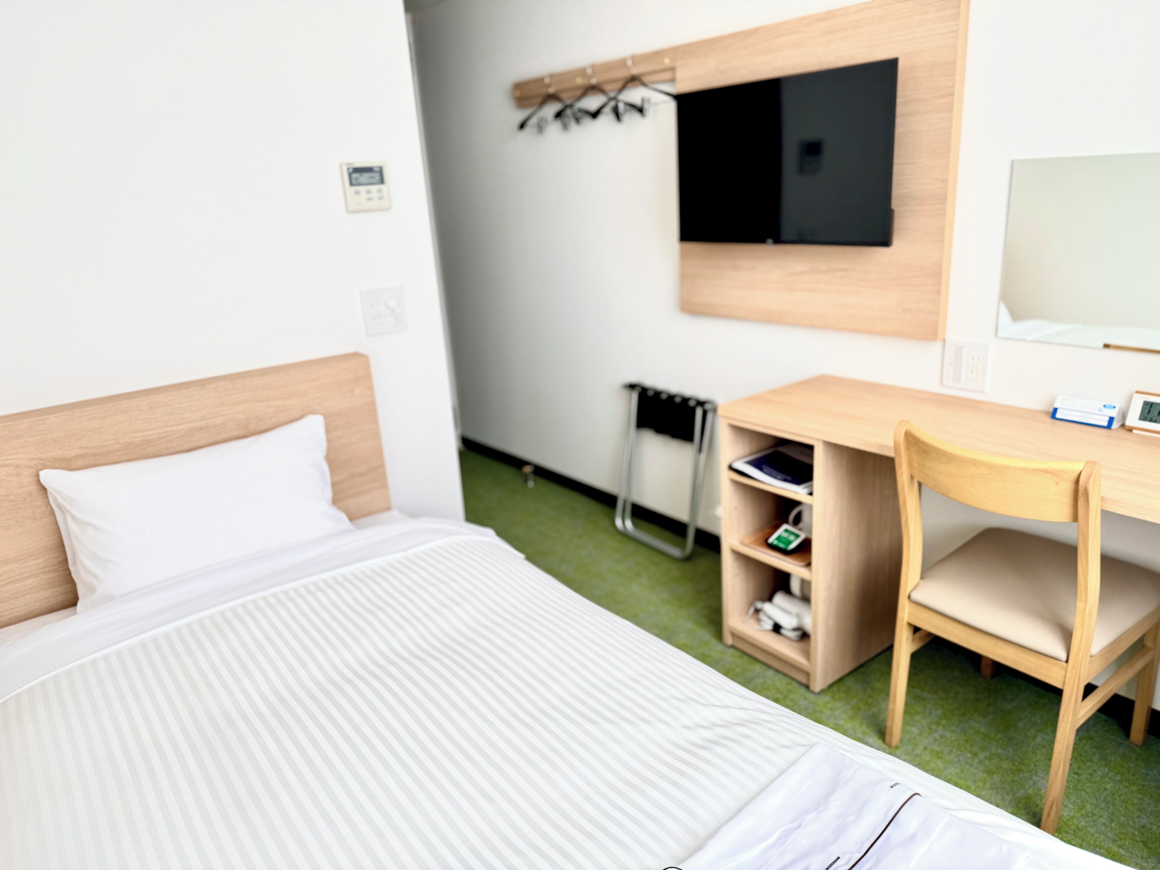 A hotel room with a bed, a desk, a chair, a TV, and a small shelf.