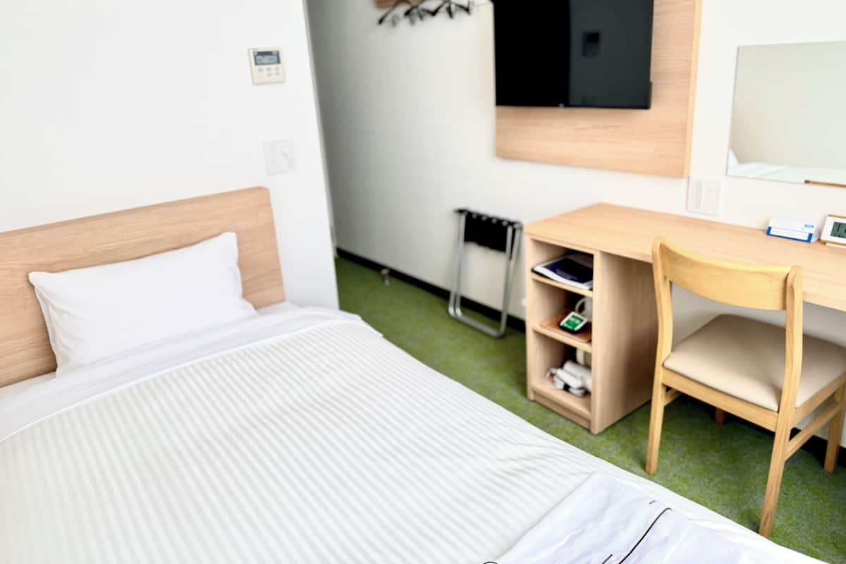 Hotellihuone, jossa on sänky, työpöytä, tuoli, televisio ja pieni hylly.
