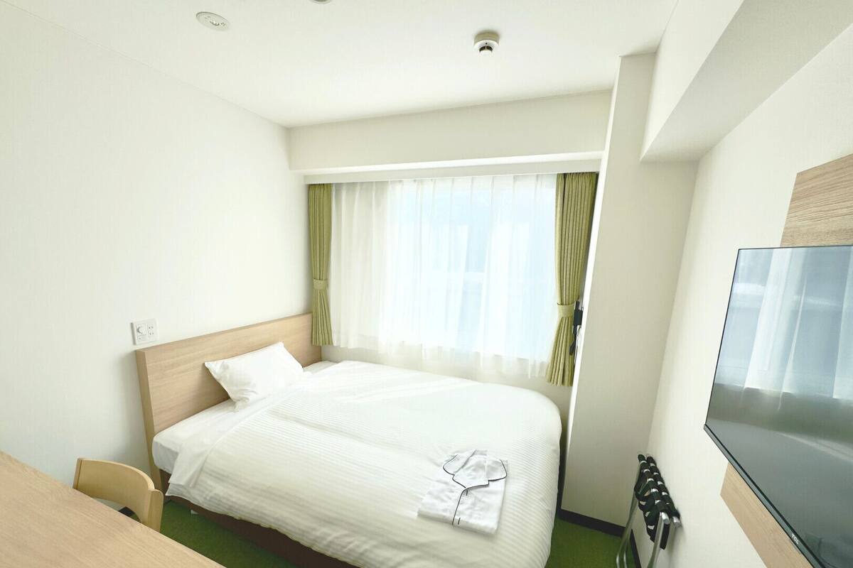 Une chambre d’hôtel avec un lit, un bureau, une télévision et une fenêtre avec des rideaux.
