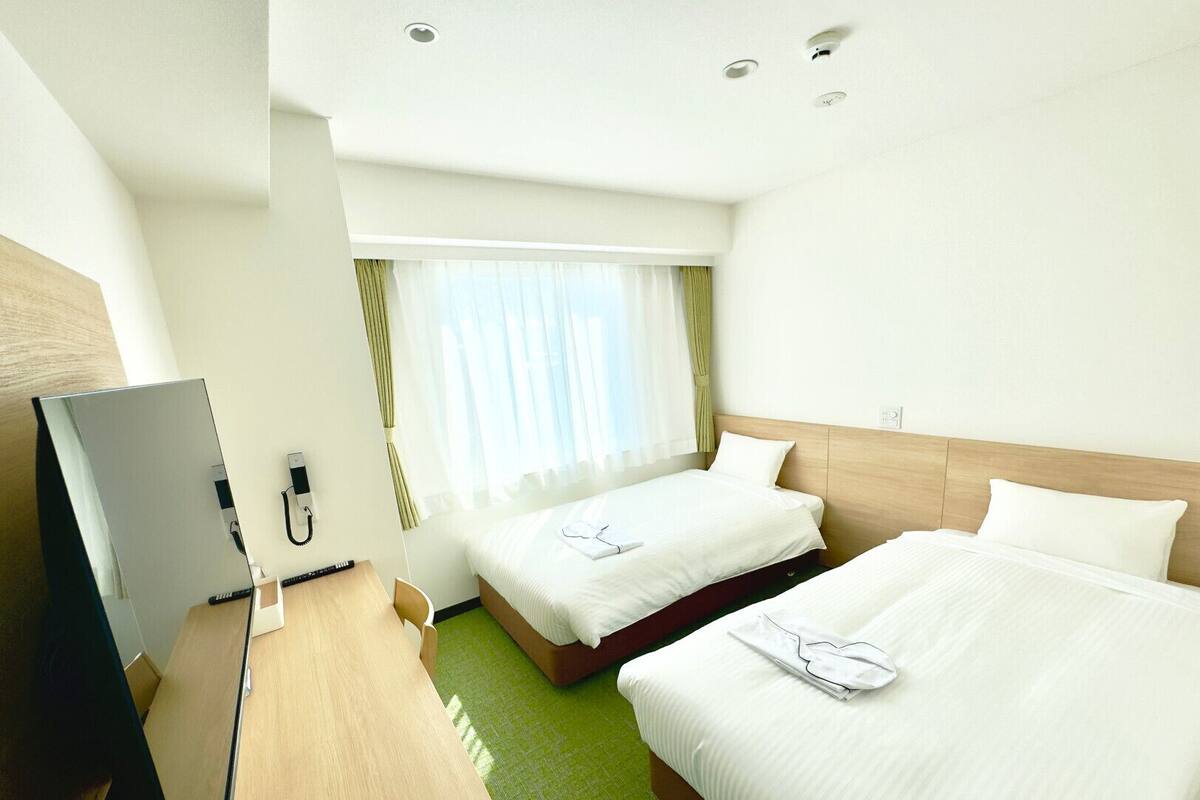 Une chambre d’hôtel avec deux lits, un bureau avec un ordinateur et une fenêtre avec des rideaux.