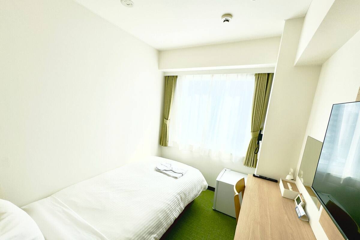 Une chambre d’hôtel avec un lit, un bureau, une télévision et une fenêtre avec des rideaux.