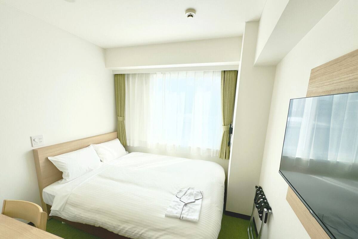 Une chambre d’hôtel avec un lit, une télévision, un bureau et une fenêtre avec des rideaux.