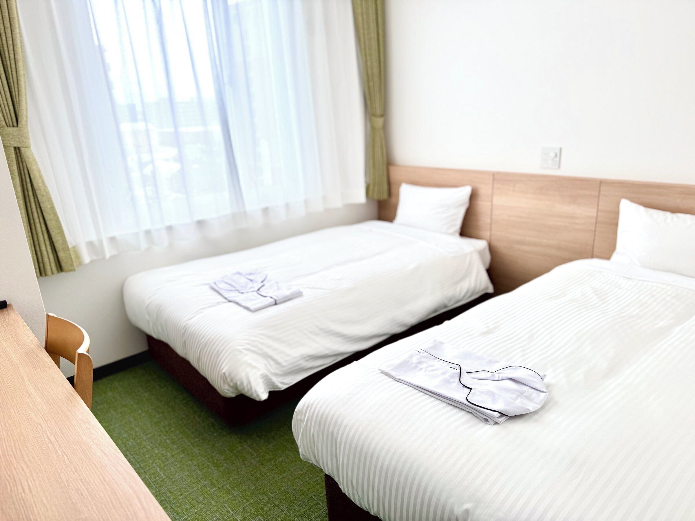 A hotel room with two beds, a desk, and a window with curtains.