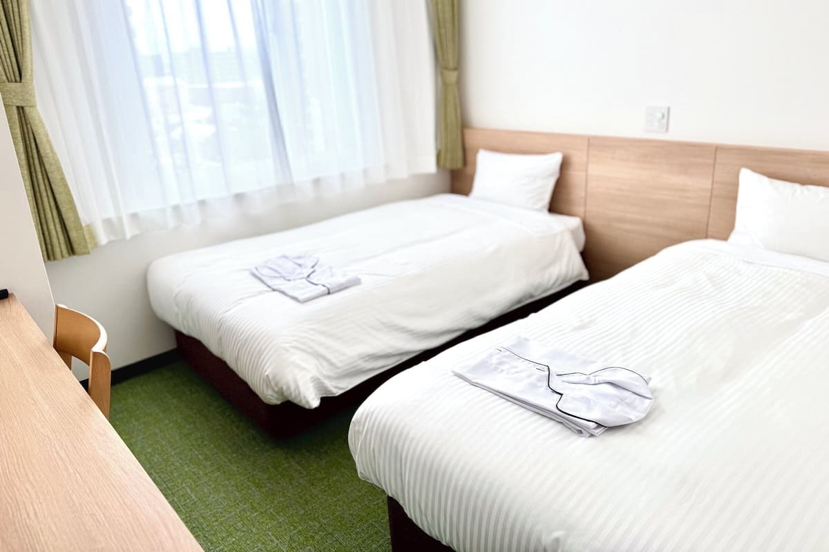 Hotellihuone, jossa on kaksi sänkyä, työpöytä ja ikkuna, jossa on verhot.