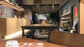 Un intérieur moderne avec une table centrale, des tabourets de bar et un comptoir où sont exposés divers articles.