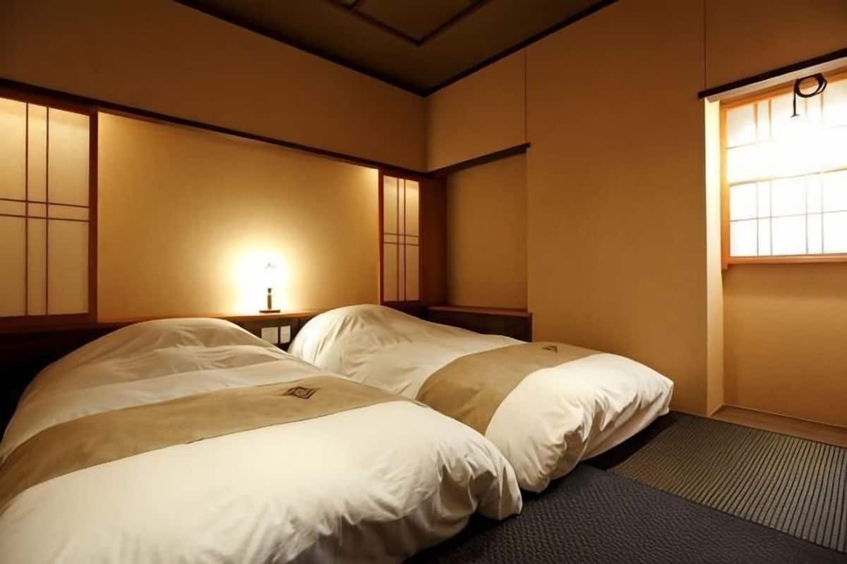 A hotel room with two beds, a bedside table with a lamp, and a window with a view.