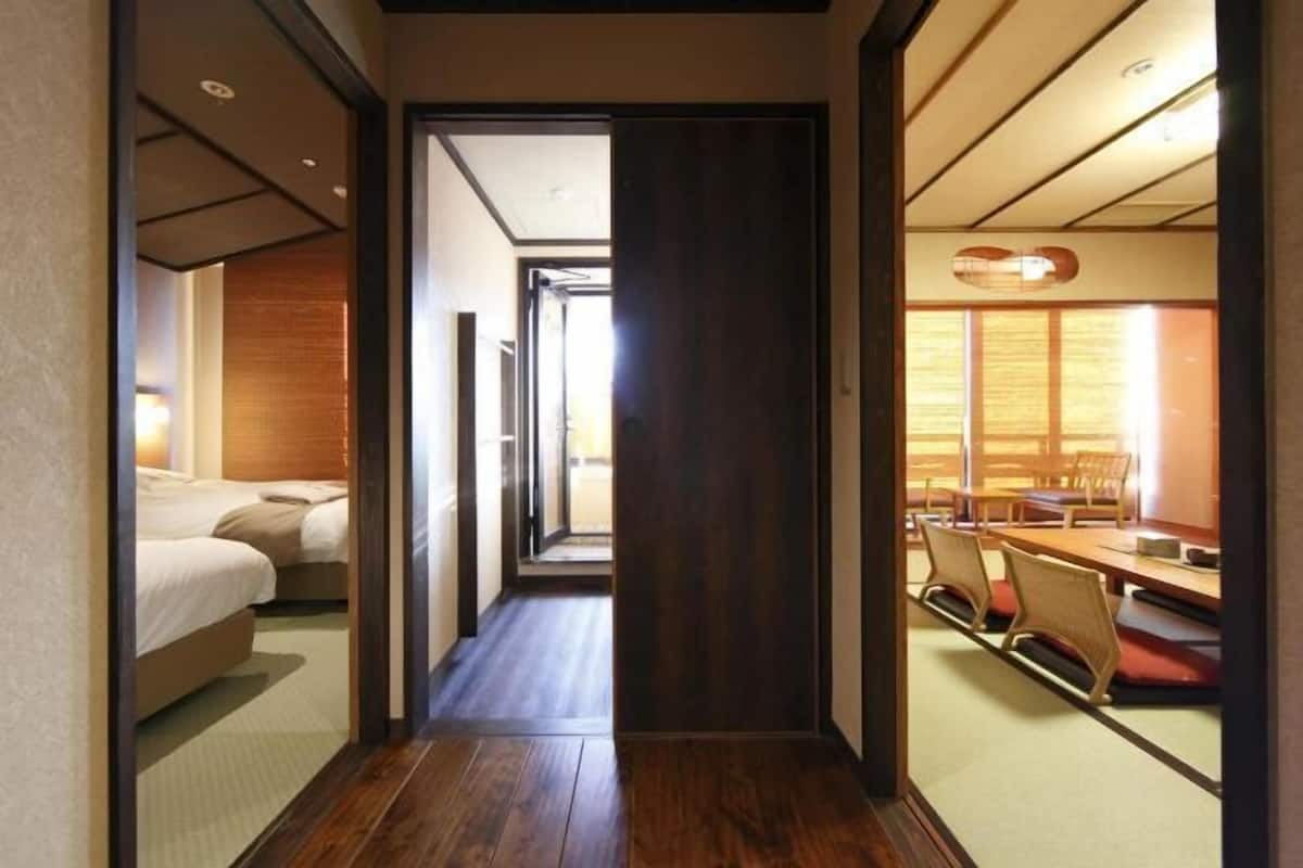A corridor leading to a room with a wooden floor, a bed, and a dining area with chairs and tables.