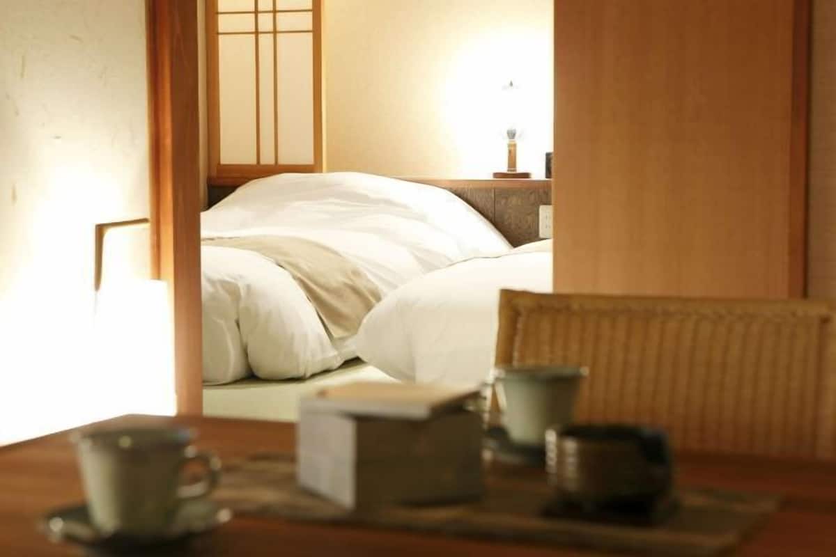 A room with a bed, a table with a cup and a box, and a lamp.