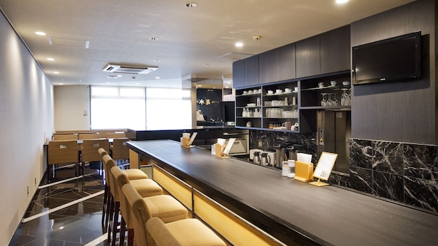 Zona de bar moderna con una barra larga, taburetes y estantes llenos de copas y botellas.