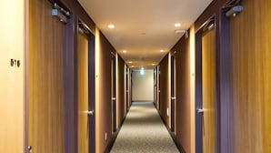 Pasillo de hotel con puertas de madera, piso alfombrado e iluminación empotrada.