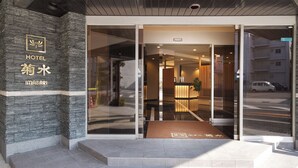 La entrada de un hotel con fachada de piedra, puertas de cristal y un área de recepción visible en el interior.