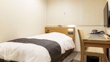 A hotel room with a bed, a desk, a chair, a television, and a small table with a kettle.