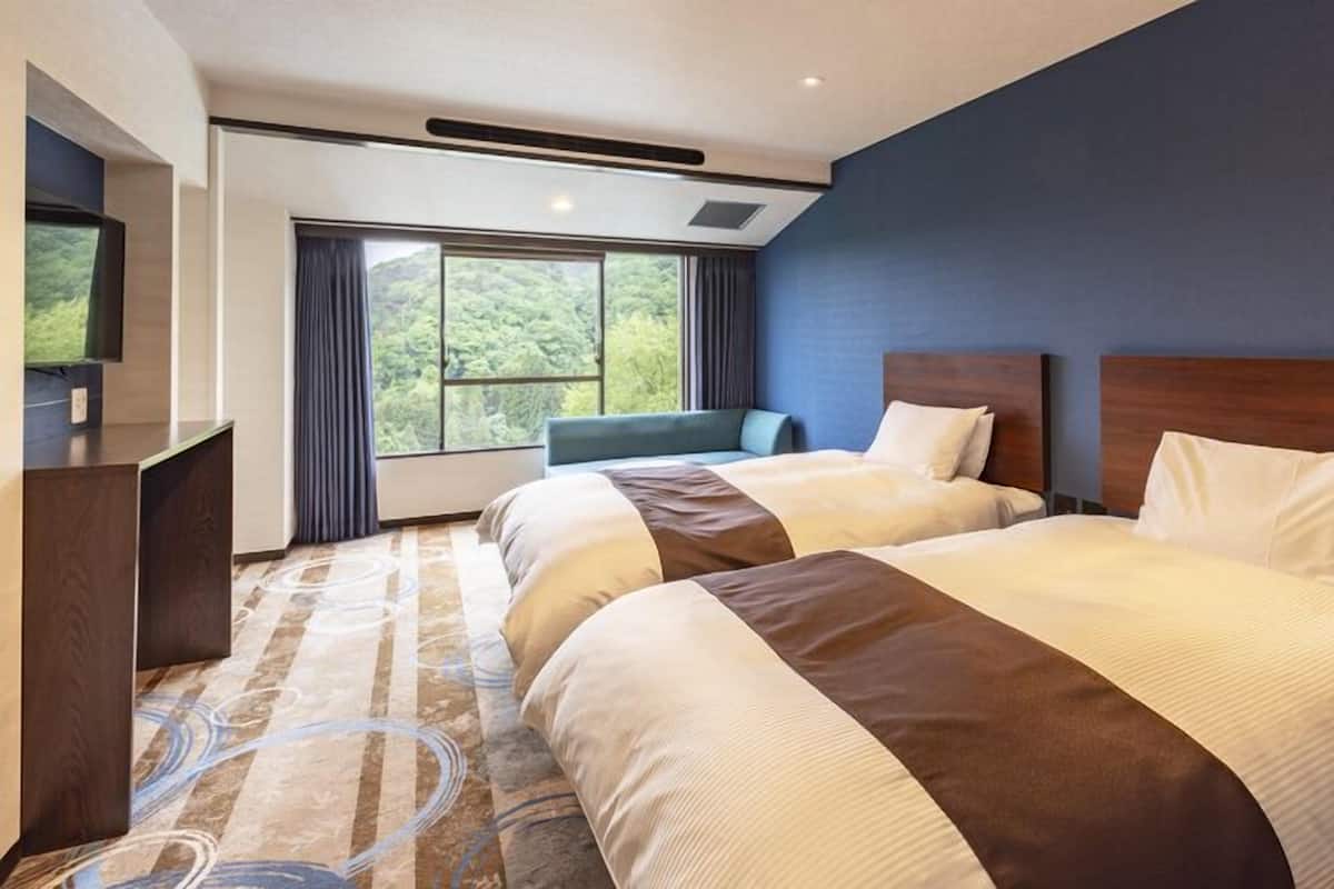 Ett hotellrum med två sängar, ett skrivbord, en stol och ett stort fönster med utsikt över träd.