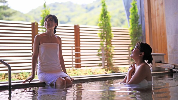 Two people in a spa-like setting with a wooden fence and greenery in the background. - Hanamaki Onsen Hotel Senshukaku (Hanamaki)