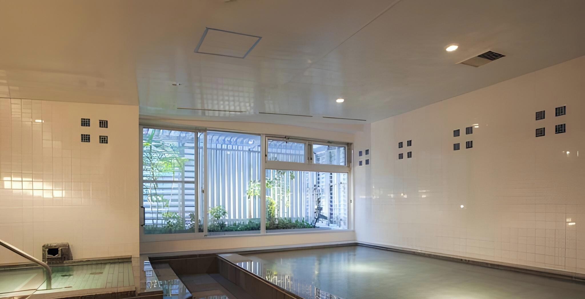 Una piscina interior moderna con ventanas amplias, un muro de azulejos y una escalera de metal.