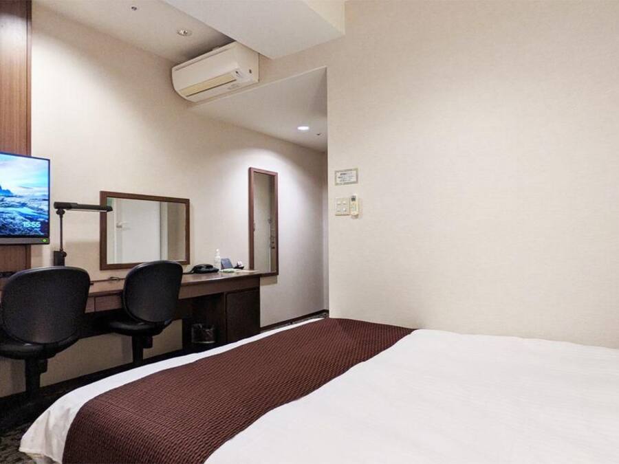 A hotel room with a bed, desk, chairs, a television, and a mirror.