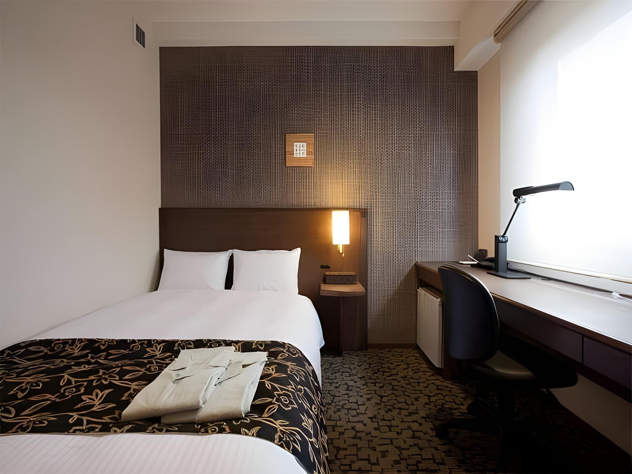 A hotel room with a bed, desk, chair, and a patterned wall.