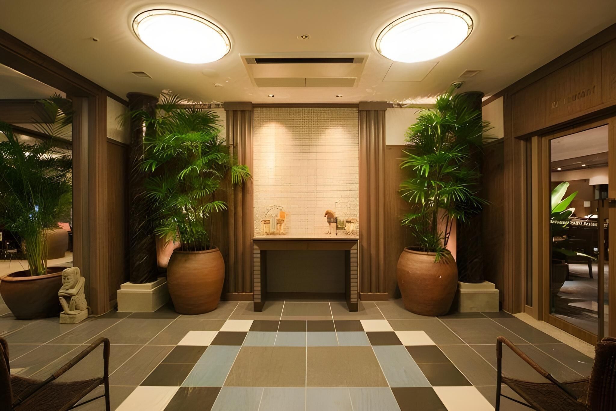 A lobby with a checkered floor, large potted plants, a statue, and a reception desk.