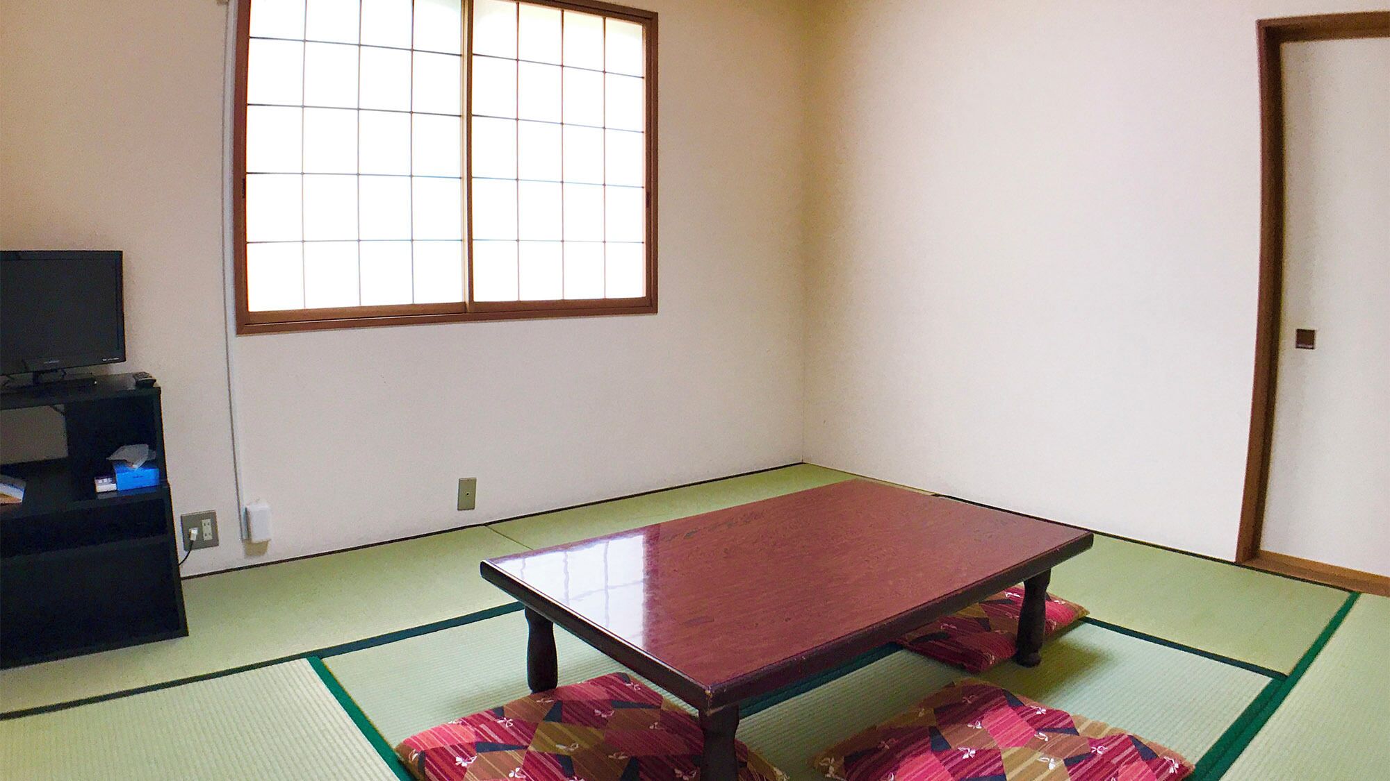 Habitación con esteras de tatami, una mesita baja, un televisor en un estante y una ventana con divisiones en cuadrícula.