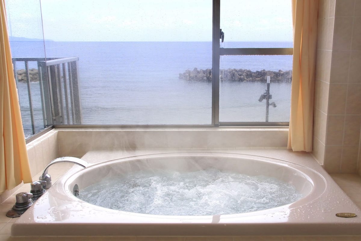 Un bain à remous avec vue sur la mer, visible par une fenêtre.