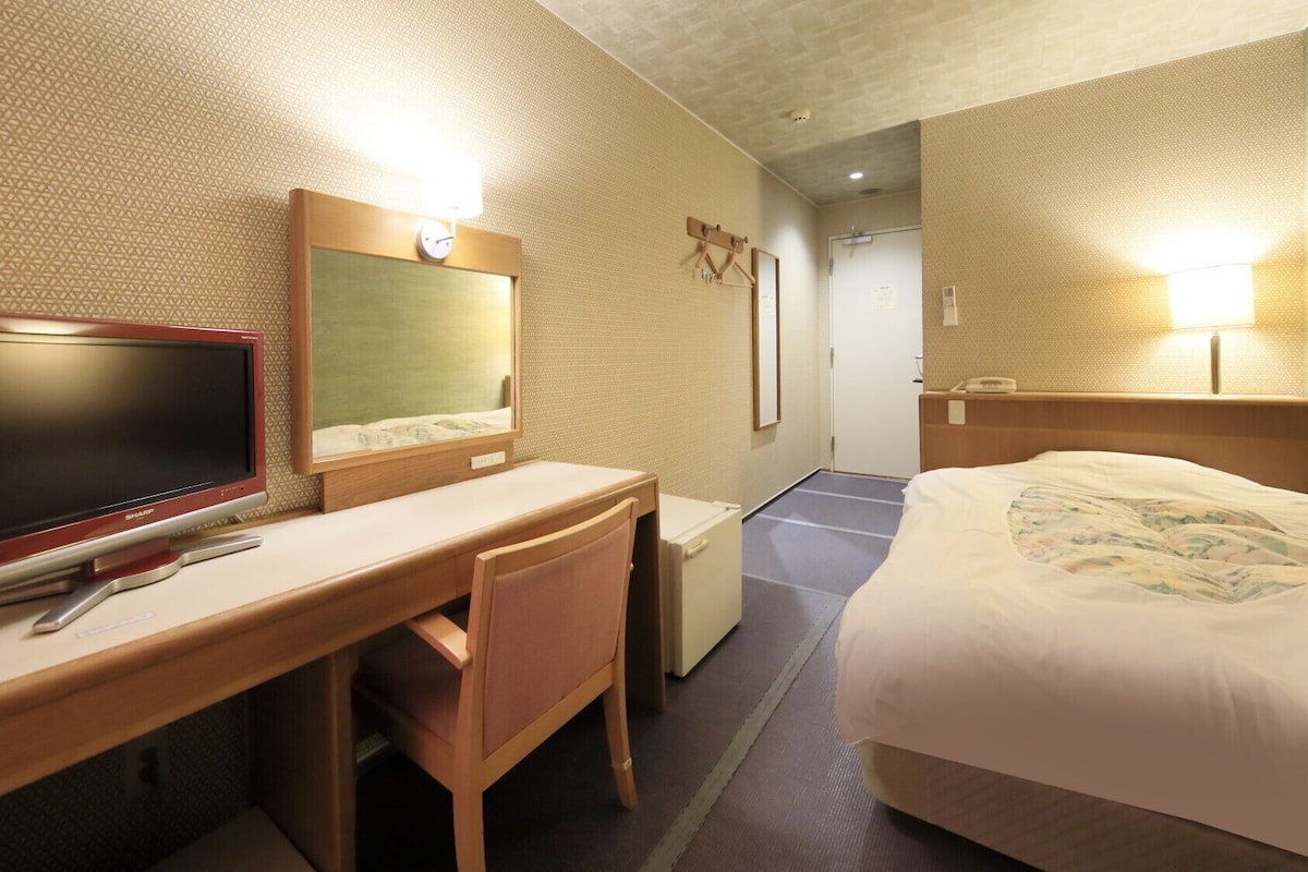 Une chambre d’hôtel comprenant un lit, un bureau avec une télévision, un miroir et une table de chevet.