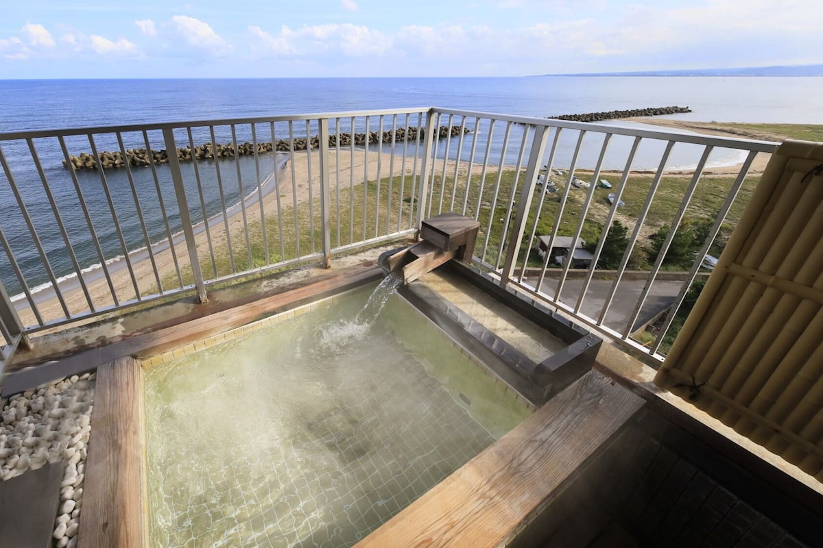 A balcony with a view of the sea, a small pool, and a wooden bench.