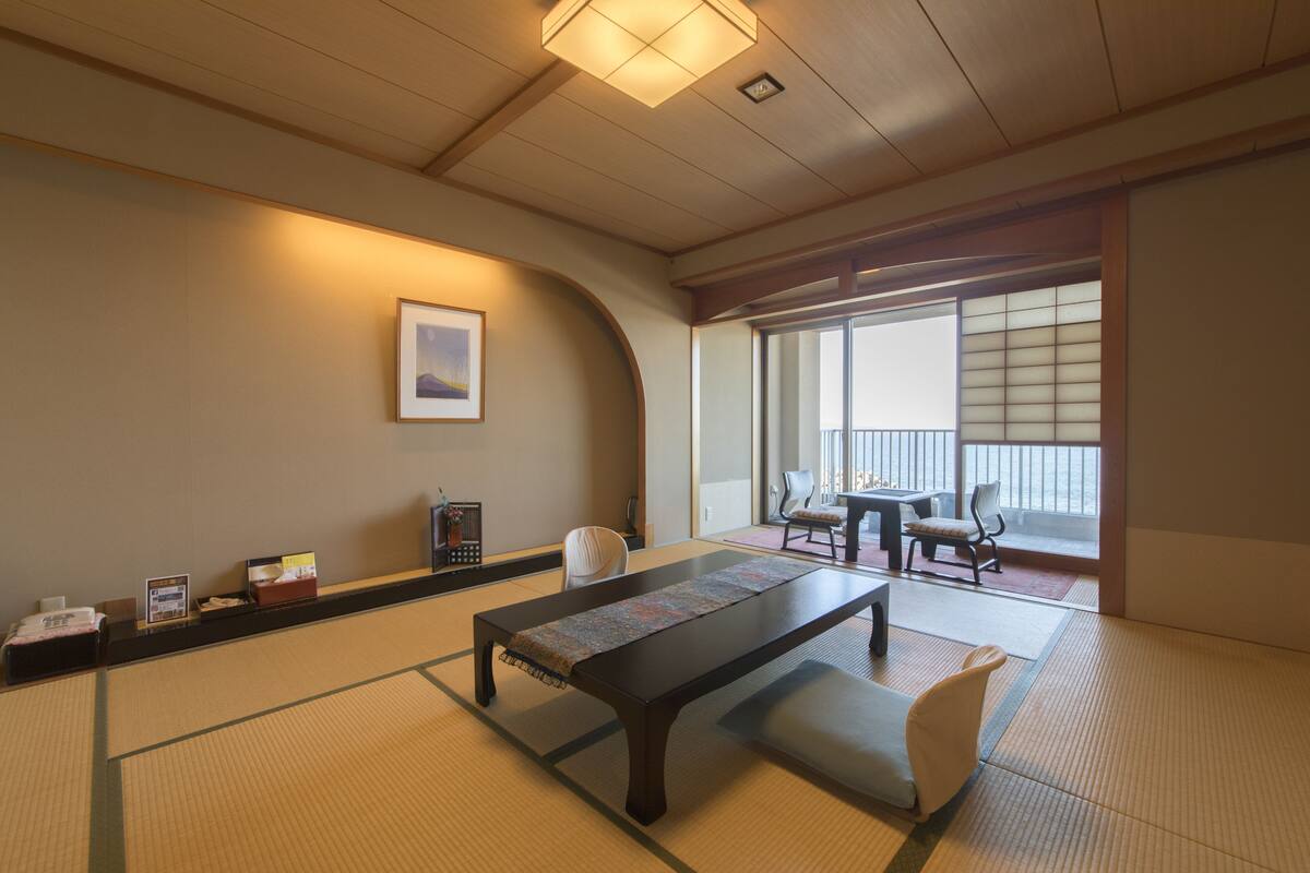 A traditional Japanese room with tatami flooring, a low table with a woven mat, and a sliding door leading to a balcony.