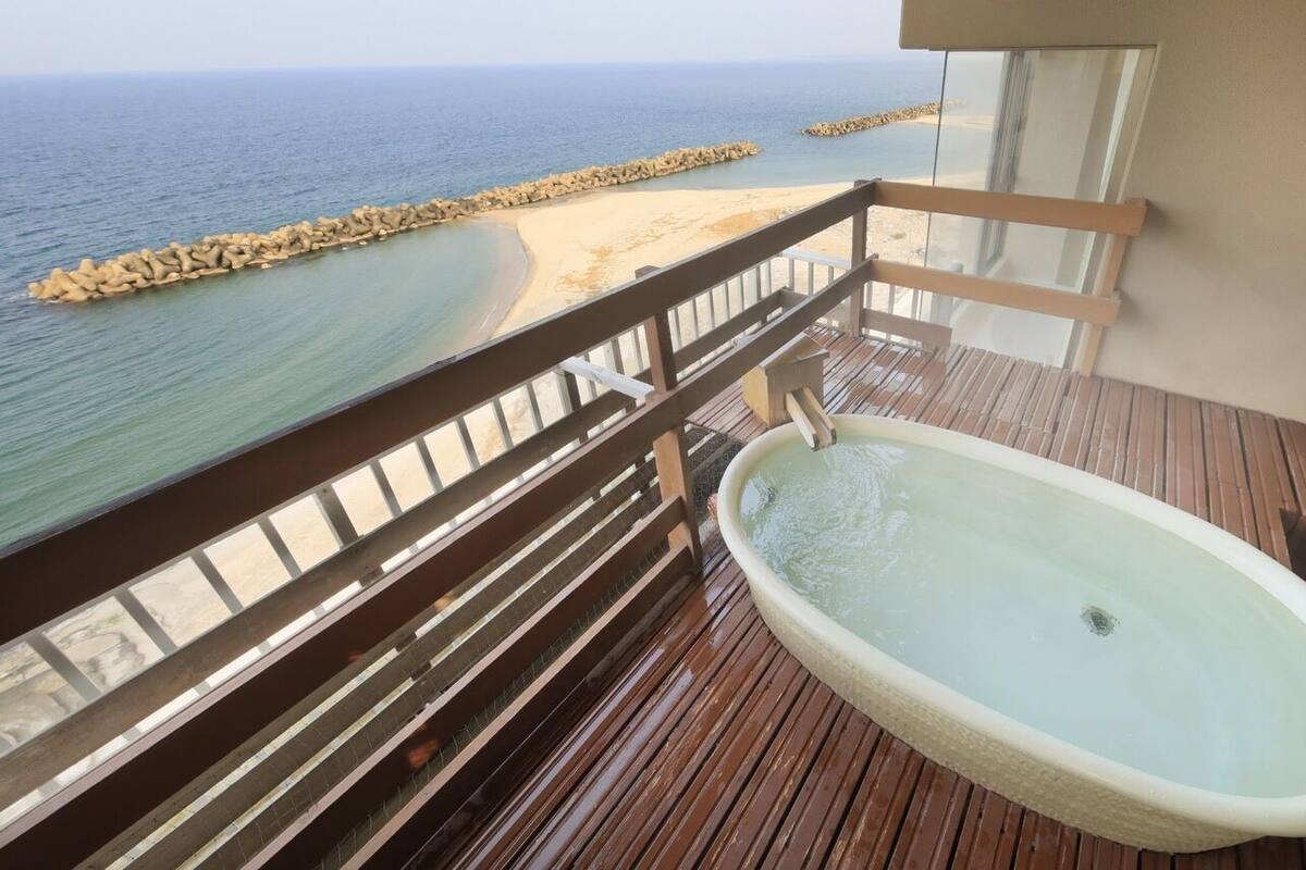 A balcony with a wooden deck, a bathtub, and a view of the beach and ocean.