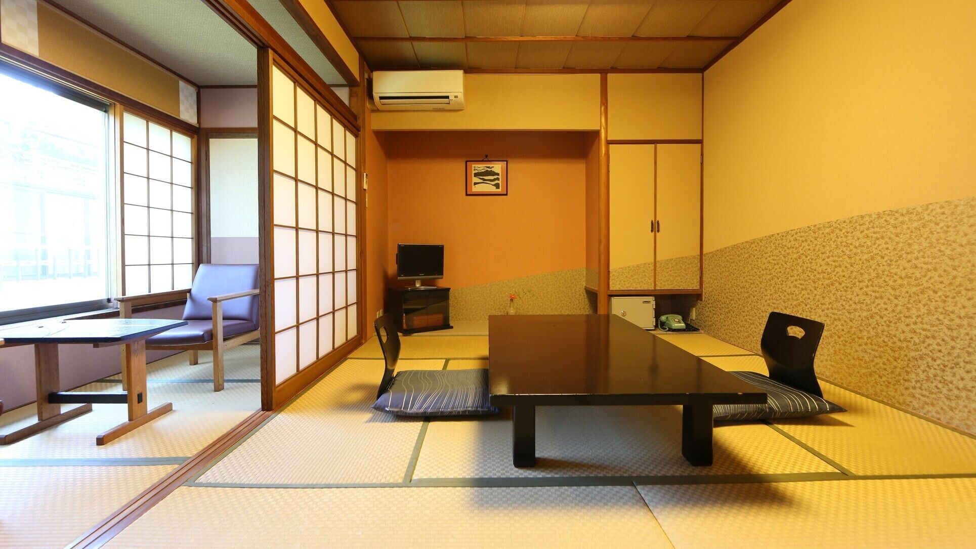 Una habitación con esteras de tatami, una mesa baja, sillas, un televisor y puertas correderas tradicionales.