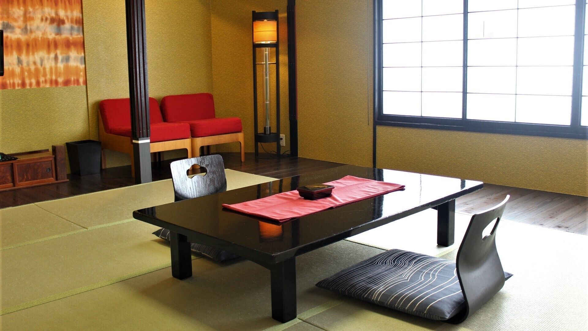 Una habitación tradicional japonesa con suelo de tatami, una mesa baja, cojines rojos y una lámpara de pie.