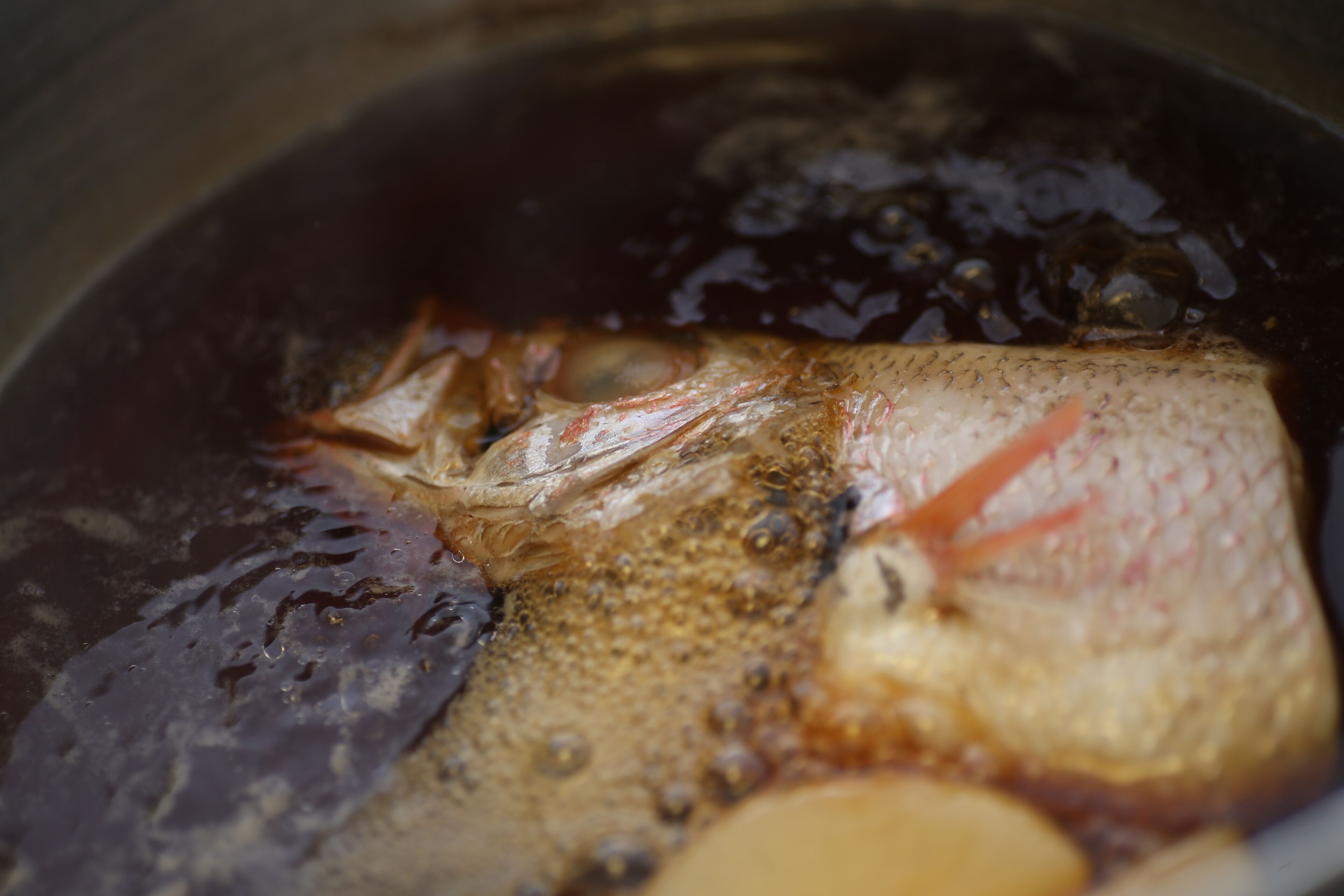 A fish in a pot with a dark liquid, possibly a marinade or cooking liquid.