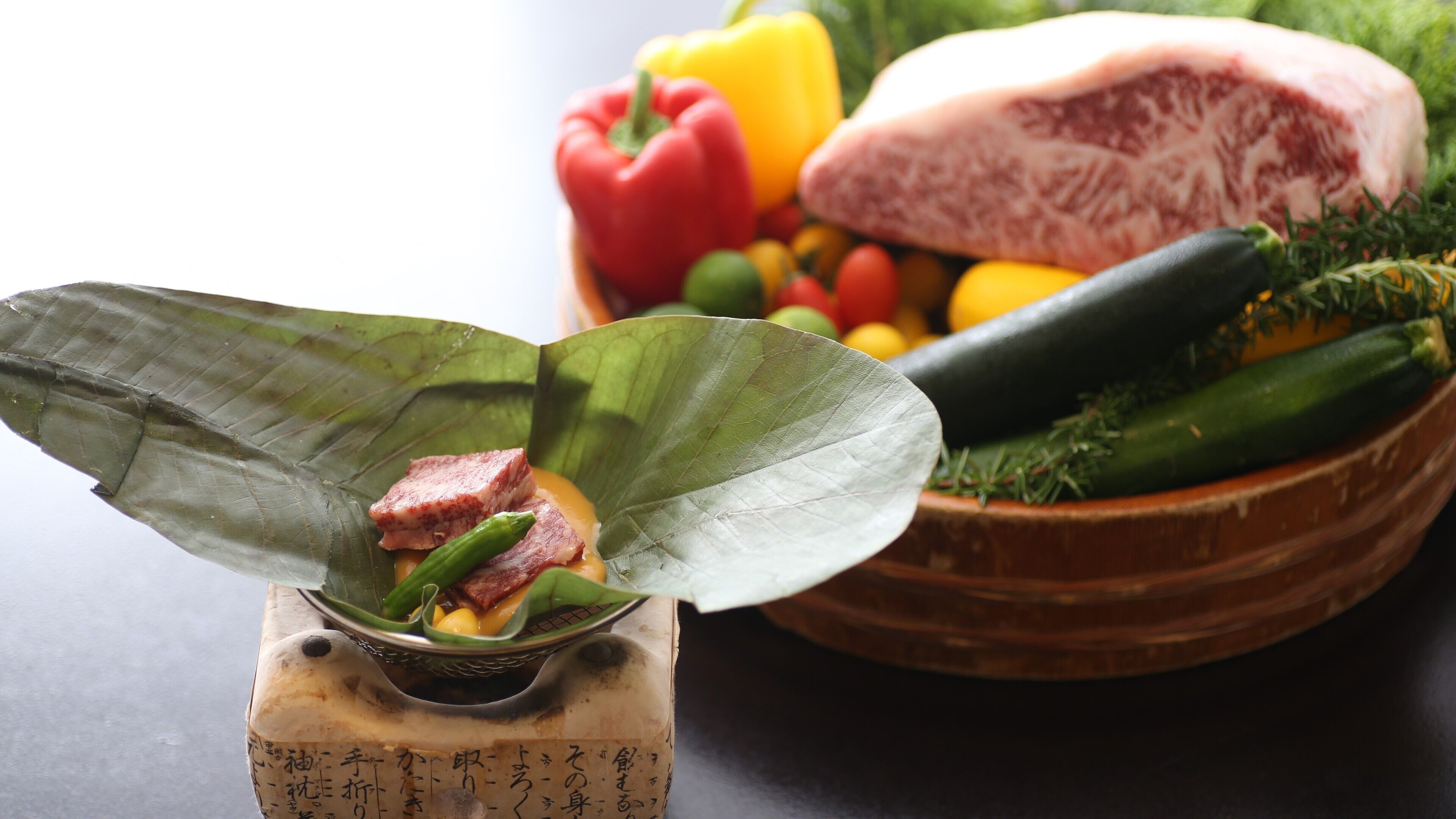 Un plato tradicional con carne y verduras, un bol de frutas y verduras variadas, y un bloque de madera con texto japonés.