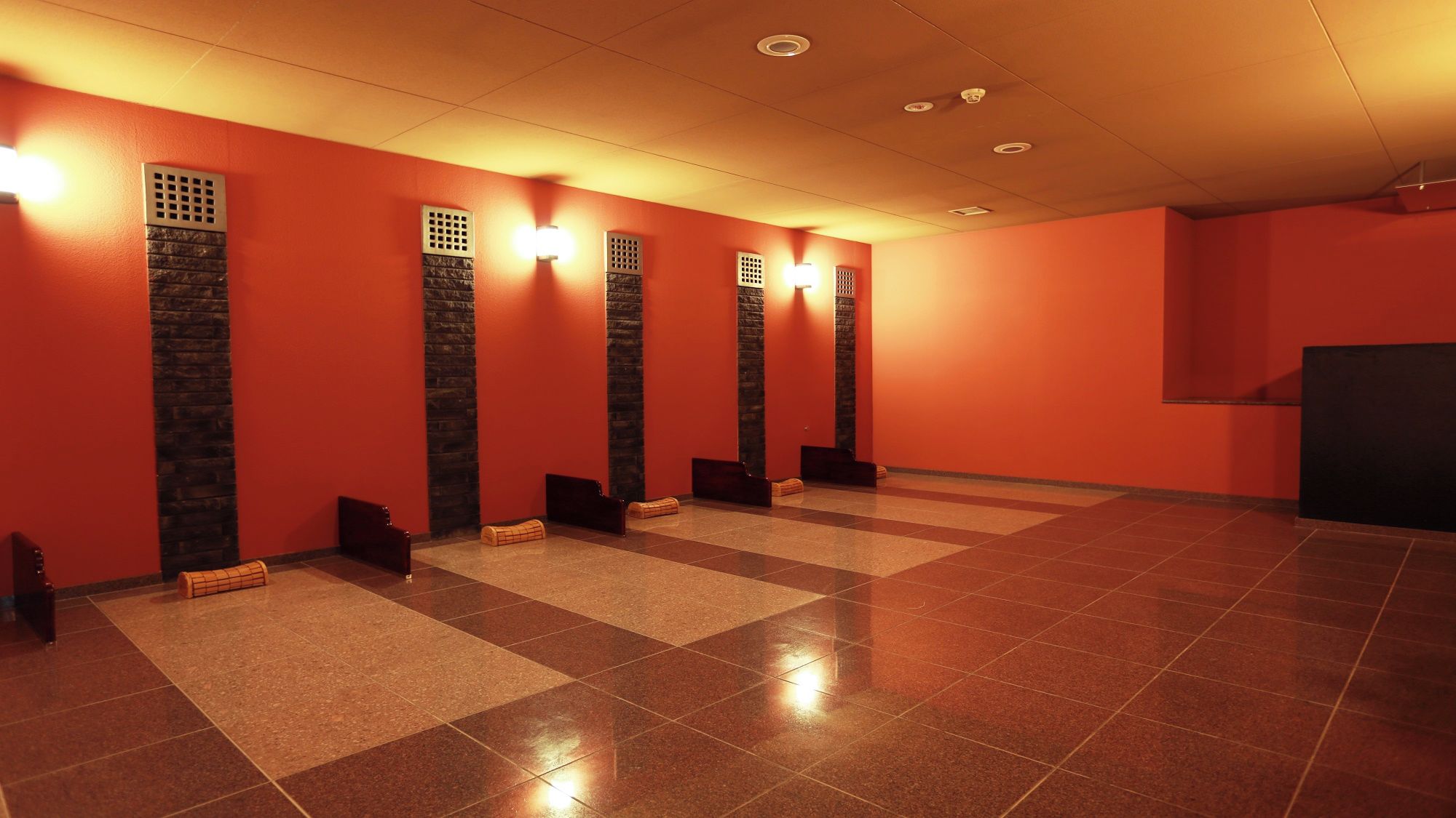 A hotel restroom with multiple sinks, tiled floors, and wall-mounted light fixtures.