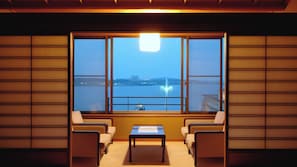 A room with a large window, two chairs, a small table, and a view of a body of water with a fountain.