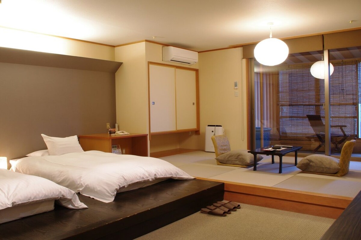 Une chambre d’hôtel avec deux lits, un canapé, une petite table et une porte coulissante donnant sur un balcon.