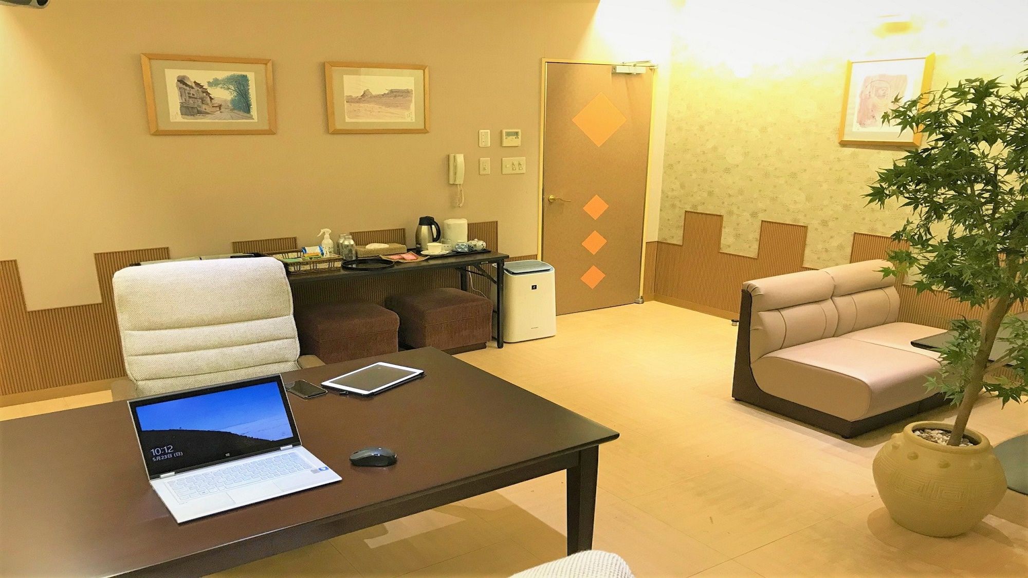 A conference room with a laptop, a tablet, a coffee maker, and a potted plant.
