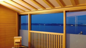 A room with a large window overlooking a body of water, a wooden bench, and a small table.