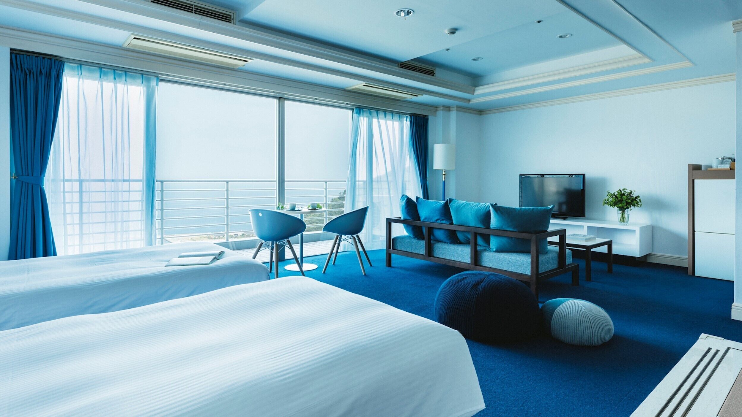 A modern hotel room with a large bed, a desk, a TV, and a balcony with curtains.
