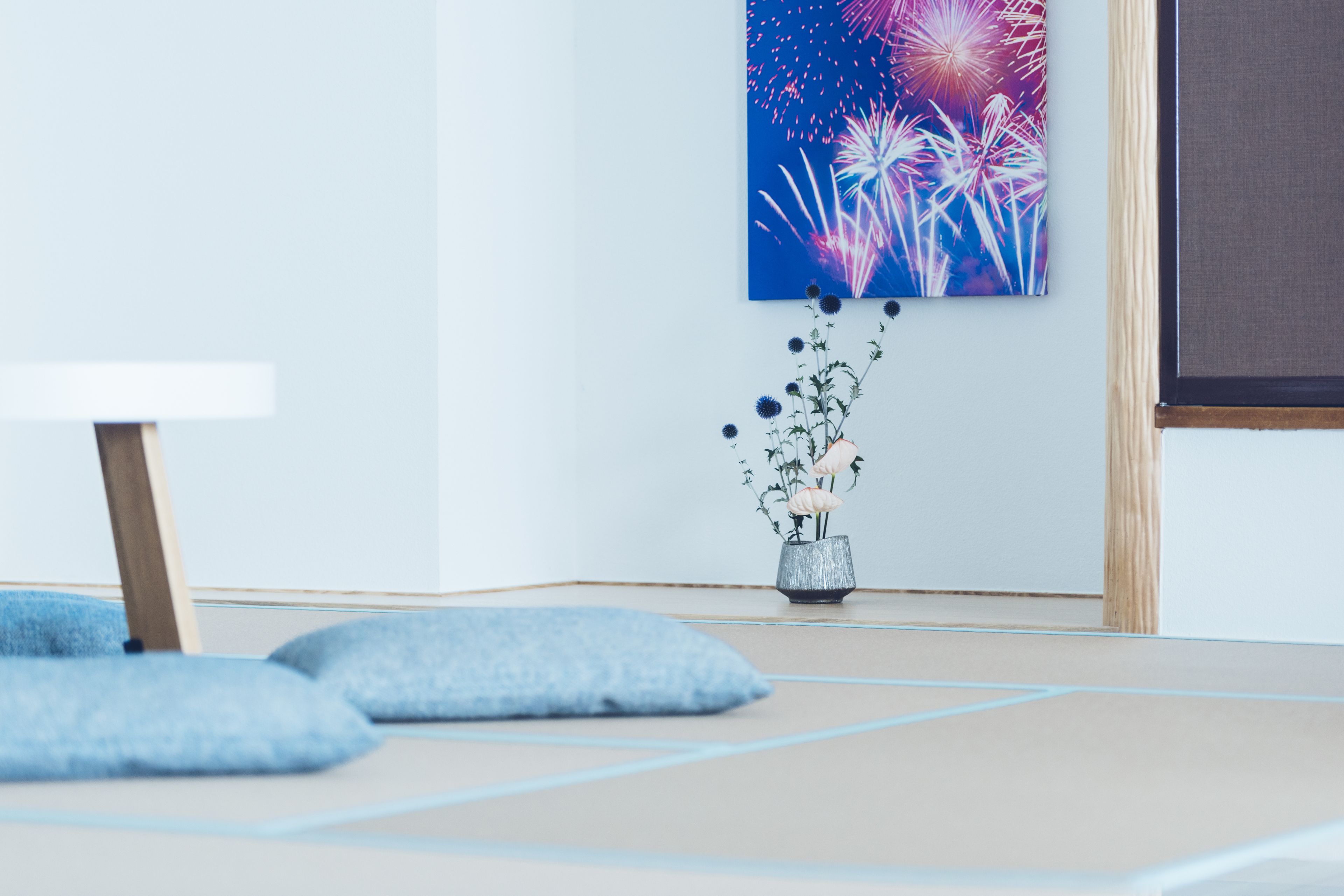Una habitación con esteras de tatami, una mesa baja, un jarrón con flores y una obra de arte en la pared que representa fuegos artificiales.
