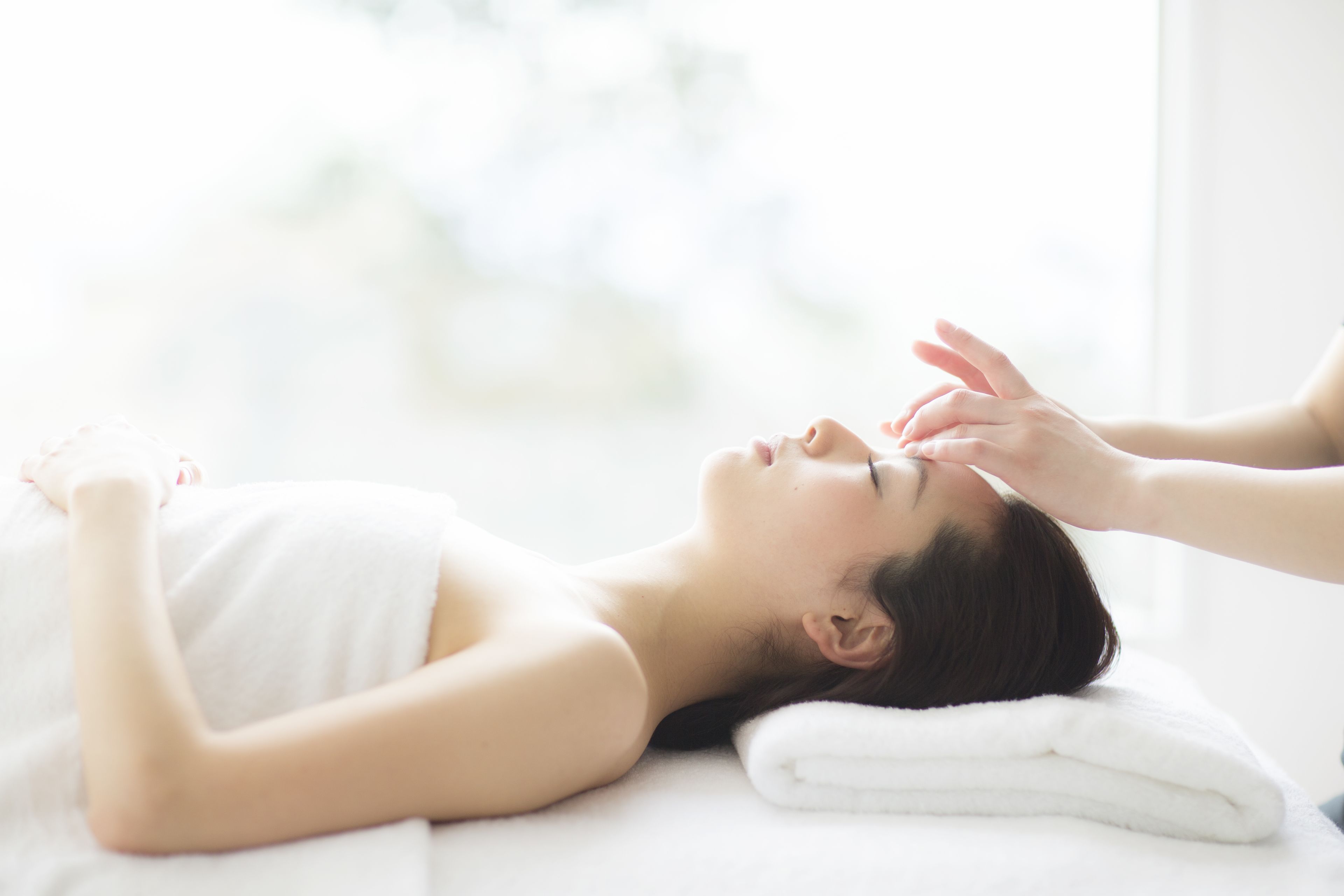 Uma pessoa deitada na cama recebendo massagem na cabeça, com uma toalha branca.