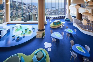 Un moderno vestíbulo de hotel con vistas panorámicas de la ciudad, zonas de estar y un techo alto con lámparas colgantes.