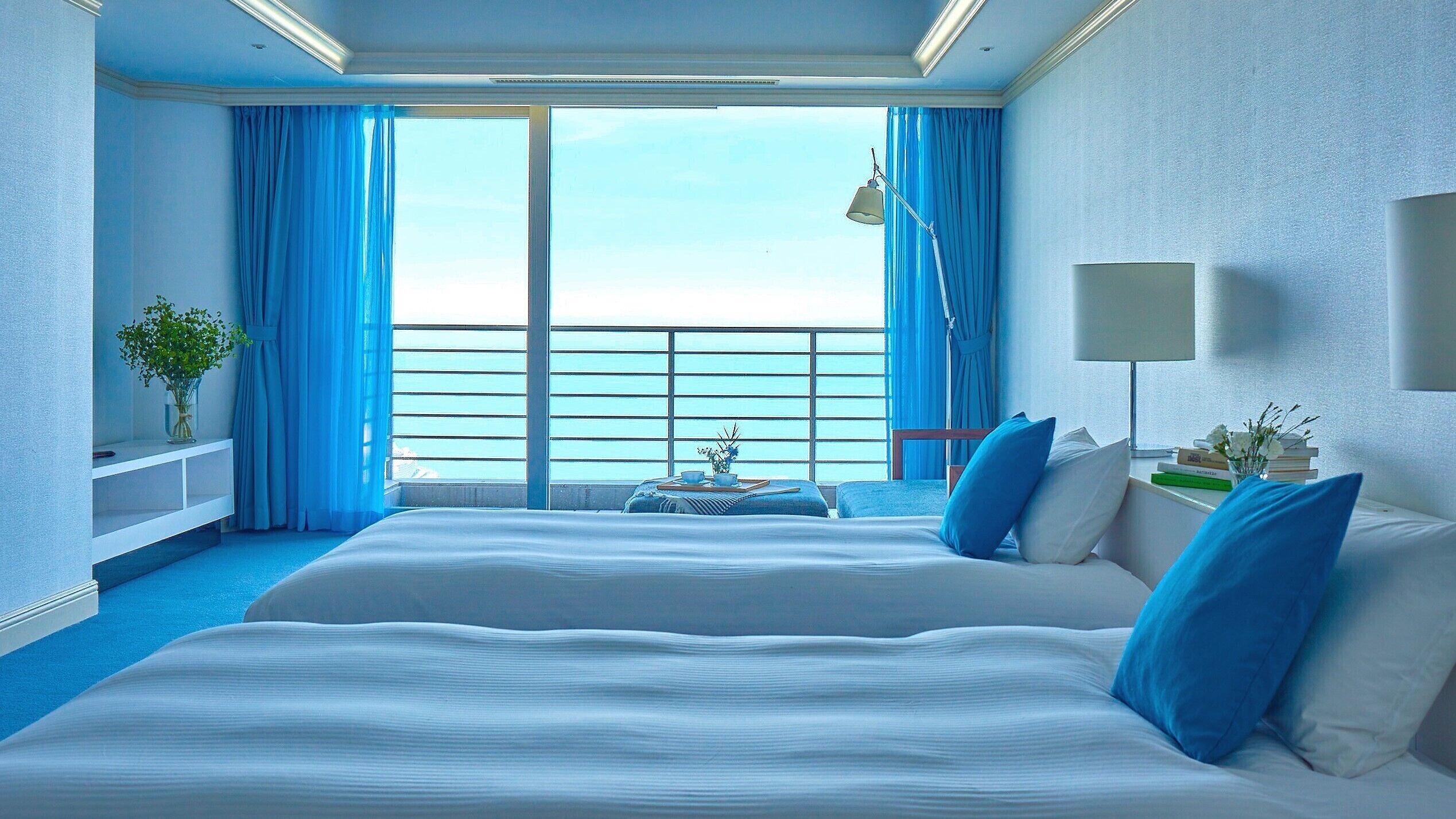 A hotel room with a large bed, a desk, a chair, a view of the sea, and a balcony.